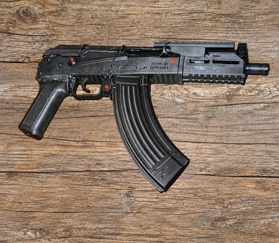 Black Draco-style AK pistol with a curved magazine, rail on top and a short handguard, lying on a wooden surface