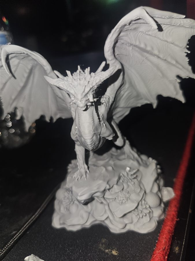 Gray 3D-printed dragon statue with wings spread, standing on a rocky base