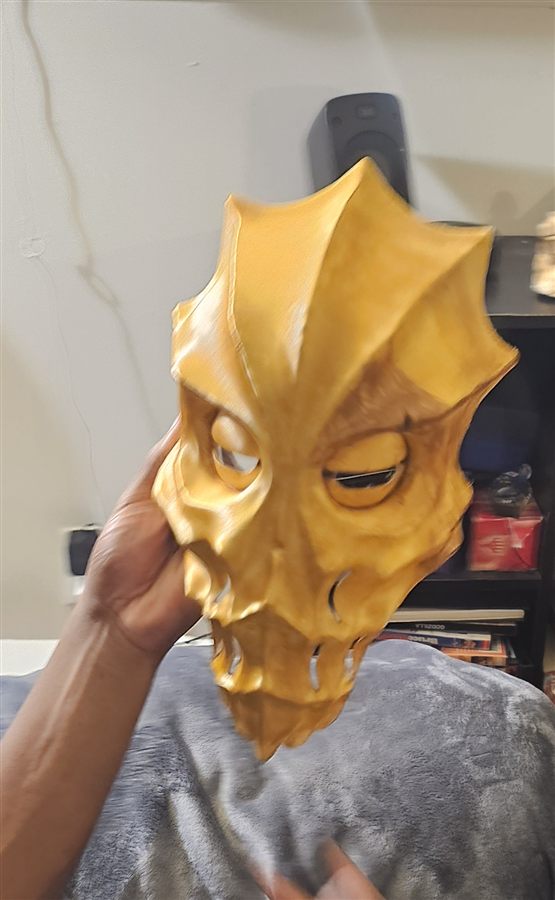 Hand holding a gold 3D-printed Skyrim mask with a spiked crest, cut-out eyes and slotted teeth