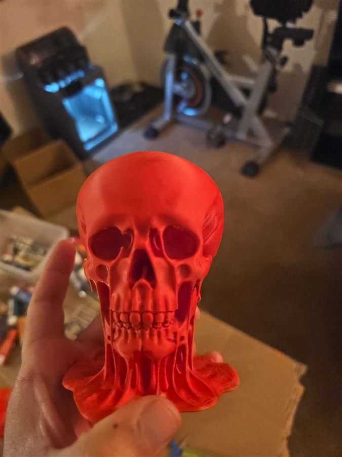Hand holding a red 3D-printed skull that melts down into a puddle at its base