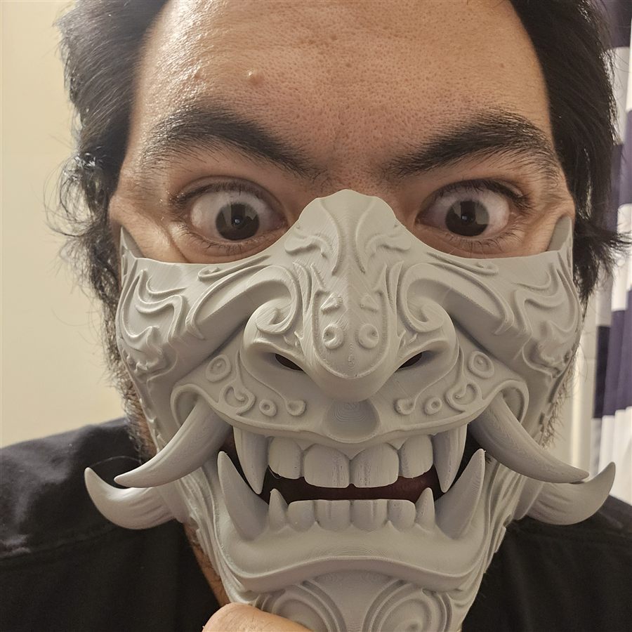 Jeremy wearing a gray 3D-printed oni mask with tusks, fangs, and carved swirl patterns