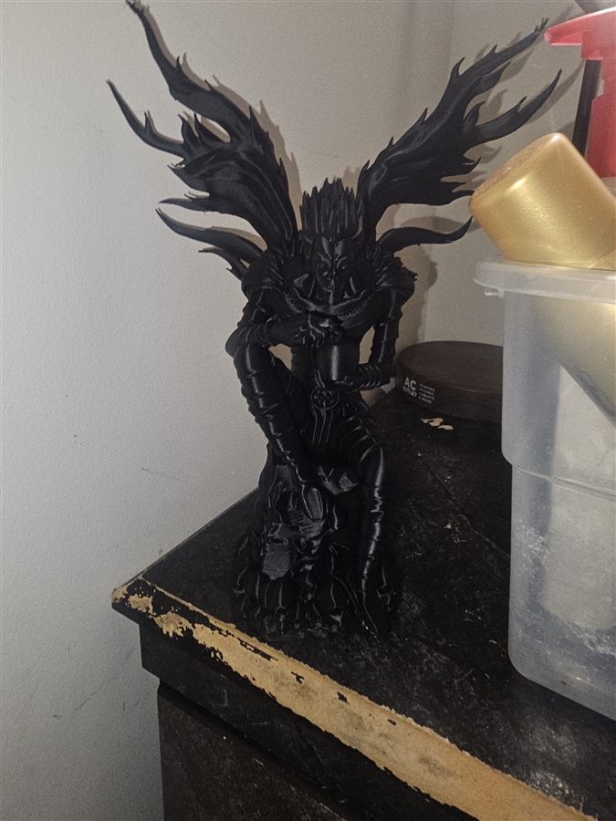 Black 3D-printed figure of Ryuk from Death Note, wings spread, crouched on a pedestal